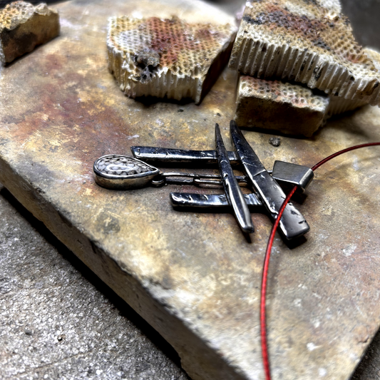 gros plan sur pendentif réalisé à partir de débris d'argent assemblés et compressés, sculptés en Torii -portail japonais d'accès au monde des esprits. Au centre de a porte est suspendu une pierre de fossile serpent sertie.
